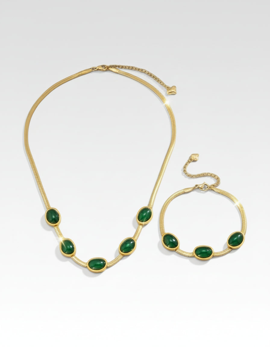 Gold necklace and bracelet set with green stones on a blue background